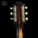 Close-up of the headstock of a guitar against a black background, showing six white tuning pegs, silver tuning machines, and a dark brown wood finish with a flame effect near the neck joint. A Tone Shop watermark is visible in the top left corner.