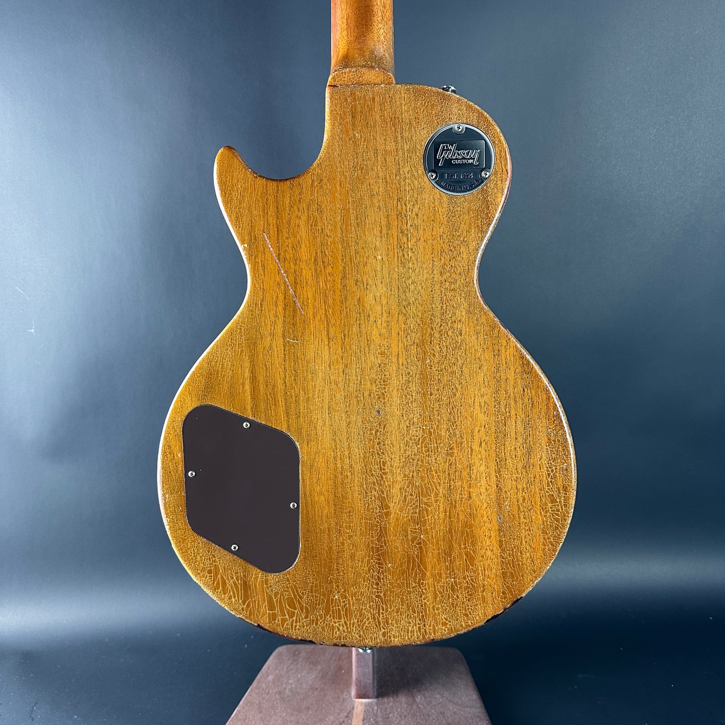 Back view of a wooden electric guitar with a brand logo on a dark gray background