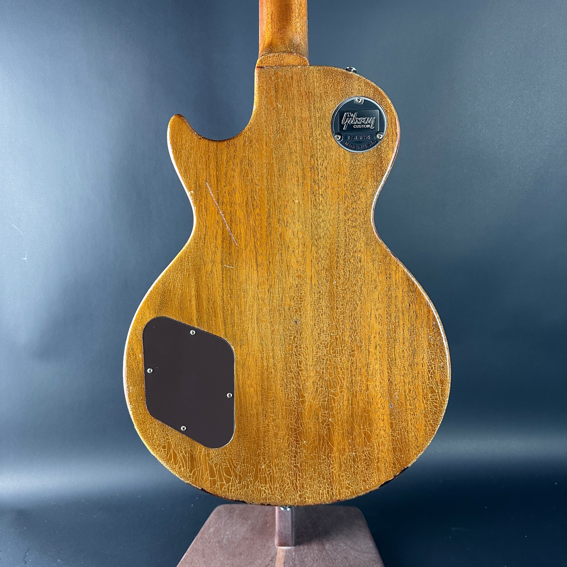 Back view of a wooden electric guitar with a brand logo on a dark gray background