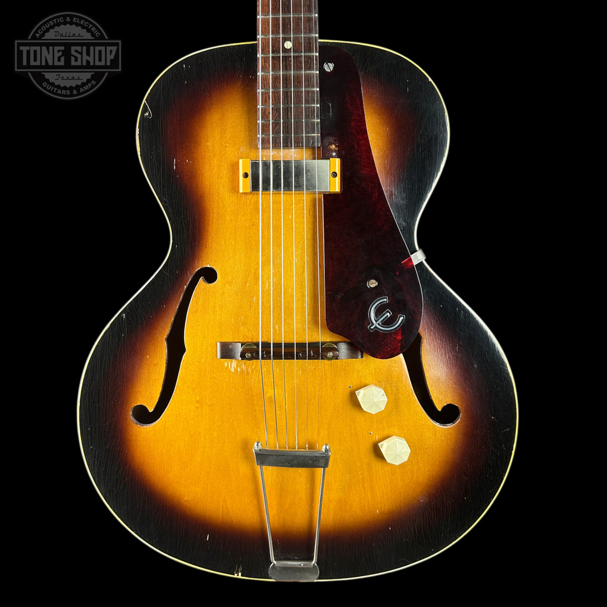 A classic hollow-body electric guitar with a sunburst finish, featuring a yellow-orange center, dark brown outer edges, and a dark reddish-brown pickguard. The guitar is shown from a front-facing perspective against a solid black background, with a 'TONE SHOP' watermark in the upper left corner.