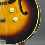 Close-up of a sunburst electric guitar body showing the wood grain, f-hole, two faceted cream knobs, and part of the bridge against a dark gray background.