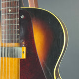 Close-up of a classic electric guitar body showing the sunburst finish, black pickguard, gold hardware, and part of the dark wood fretboard against a neutral gray background.