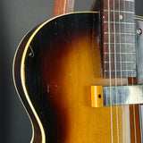 Close-up of a vintage electric guitar body showing a sunburst finish that transitions from black to amber brown, with a dark wood fretboard and gold hardware.