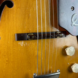 Close-up of a wooden electric guitar body with six strings, a dark bridge, and light-colored control knobs.