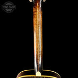 Close-up of the neck of a wooden stringed instrument, likely a mandolin or small guitar, showing a glossy brown wood finish with visible grain and a white peg head, set against a solid black background.