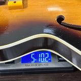 Close-up of a digital scale displaying the weight of a sunburst electric guitar body, resting on a dark wooden surface.
