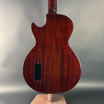 Back view of a wooden guitar on a stand with a gray background