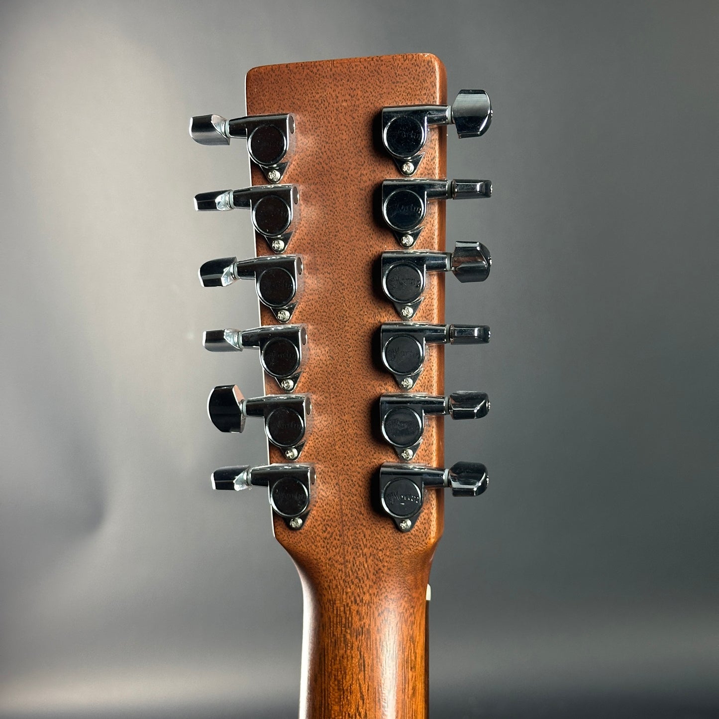 Close-up of a guitar headstock with 12 tuning pegs on a gray background