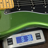 A close-up of a green electric guitar body resting on a digital scale showing a weight of 8 lb 38 oz.