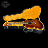 An acoustic guitar with a sunburst finish displayed inside an open black hard case with a bright orange-yellow velvet interior, set against a solid black background.