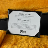 A Gibson Custom Certificate of Authenticity card inside a black frame, placed on a yellow faux fur surface next to a black case.