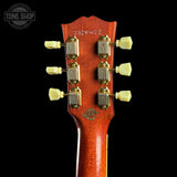 Close-up of the headstock of a guitar, showing six cream-colored tuning pegs, gold-toned tuning machines, and a reddish-brown wood backplate with 'Tone Shop' branding and serial number 2329162.