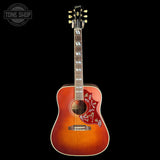 A Gibson acoustic guitar with a sunburst finish, featuring floral inlays on the lower bout and a dark headstock, shown against a solid black background with a Tone Shop watermark in the top-left corner.