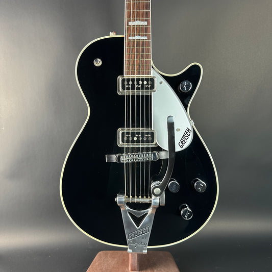 Black electric guitar with a white pickguard on a gray background