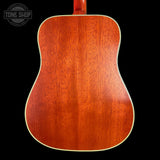 The back of an acoustic guitar with a glossy reddish-brown wood finish and a cream-colored edge trim, shown against a solid black background.