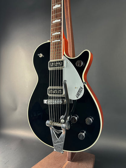 Black electric guitar with a brown pickguard on a gray background