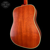 Close-up of the back of an acoustic guitar showing a rich reddish-brown wood finish and a cream-colored edge trim, set against a solid black background with a Tone Shop watermark in the top left.
