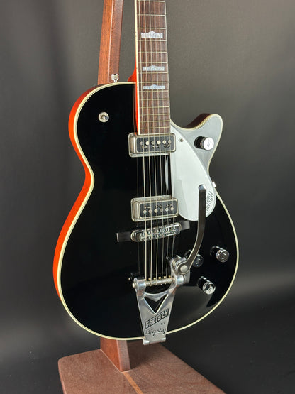 Black electric guitar with a red pickguard on a dark background