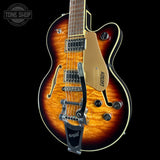 A Gretsch double-cutaway electric guitar with a natural flame maple top, featuring a gold body, black hardware, and a black bridge, shown against a solid black background.