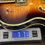 A close-up of a sunburst electric guitar body resting on a digital scale showing a weight of 7.71 lbs (3.