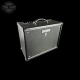 A black BOSS guitar amplifier with a textured front grille and silver hardware, shown at an angle against a solid black background. A Tone Shop watermark is visible in the top-left corner.