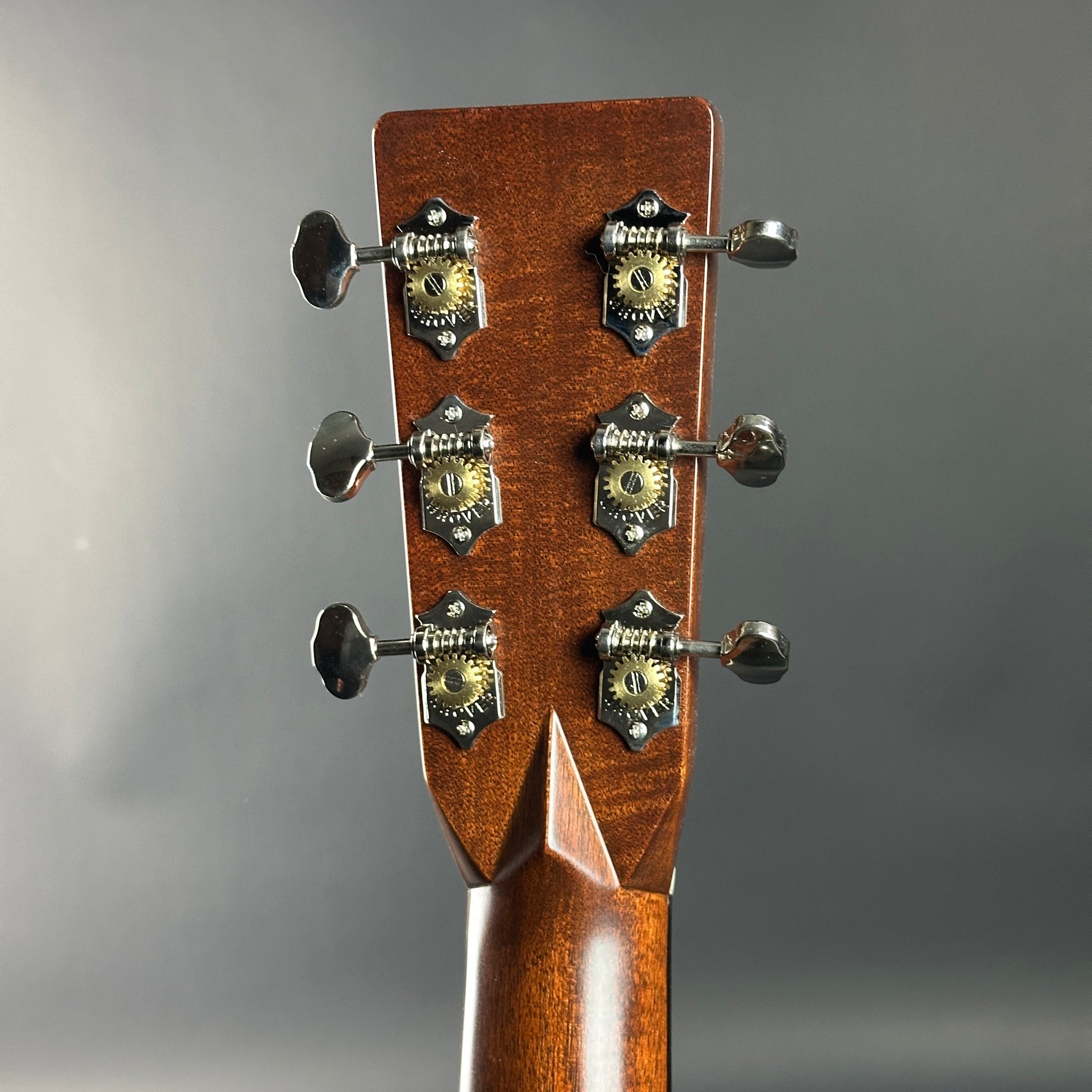 Close-up of a guitar headstock with tuning pegs on a gray background