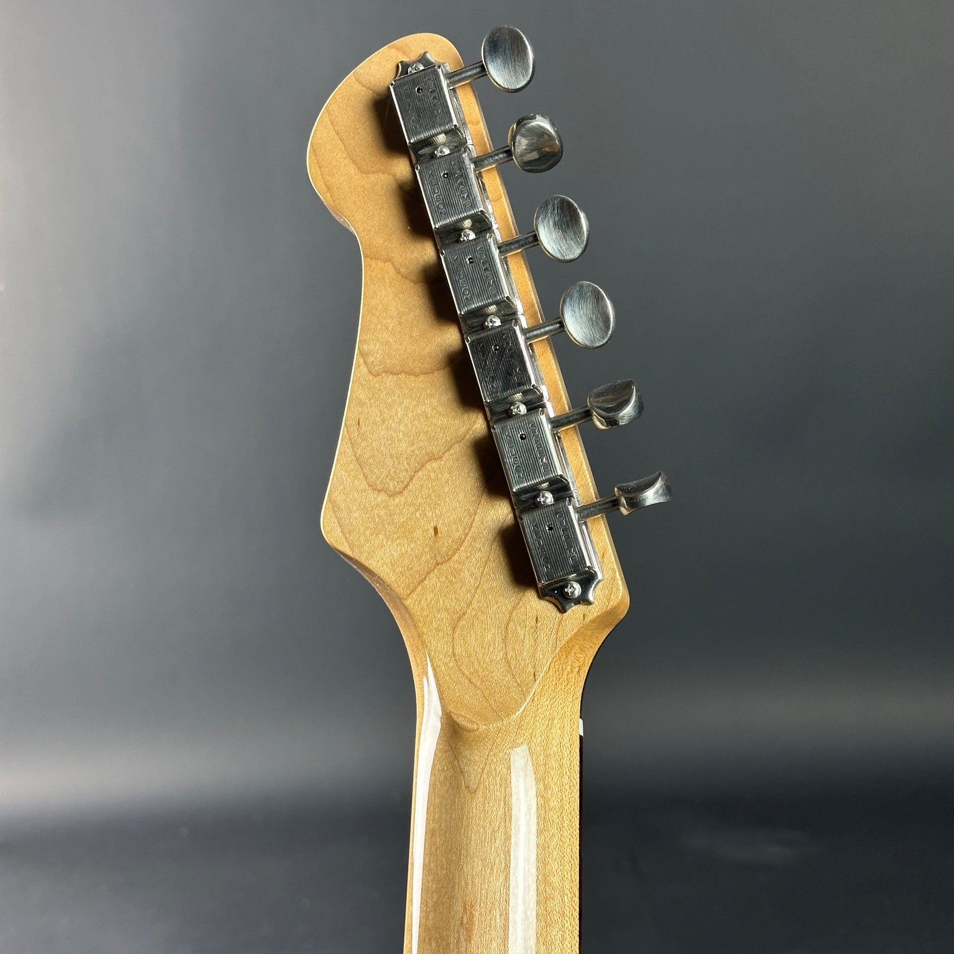 Close-up of a guitar headstock with tuning pegs on a gray background