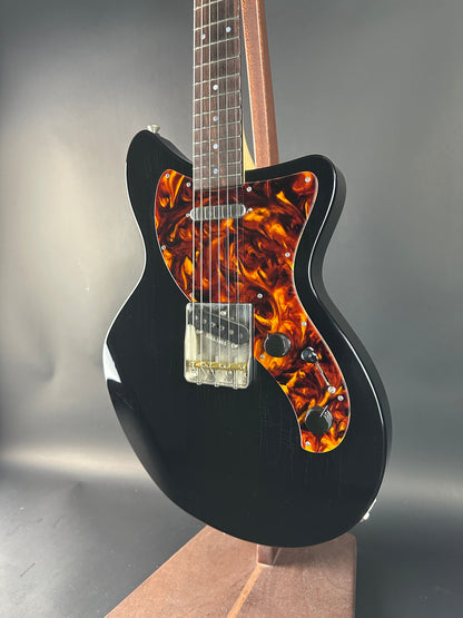 Black electric guitar with tortoiseshell pickguard on a reflective surface