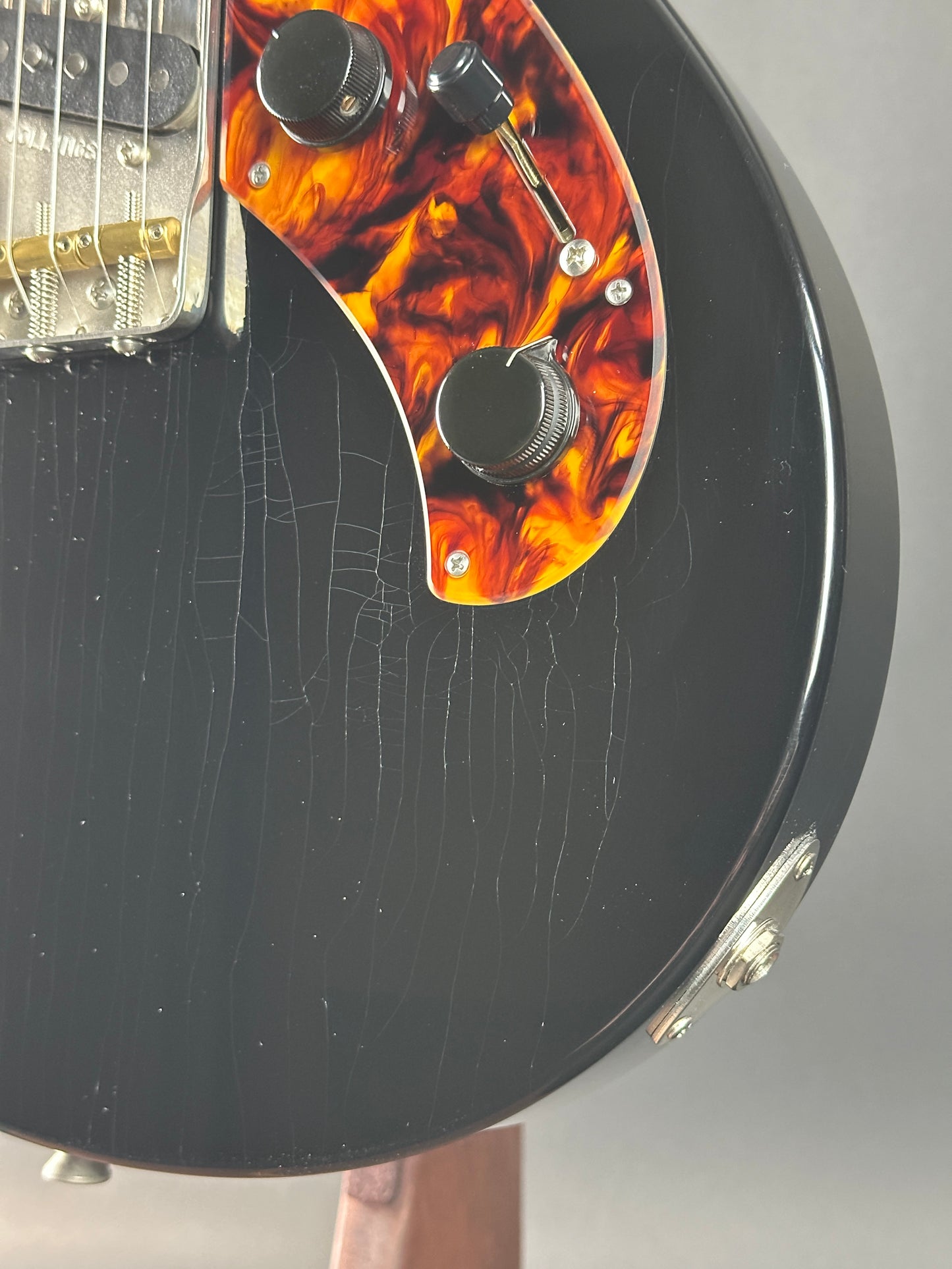 Close-up of a guitar headstock with tortoiseshell inlay on a gray background