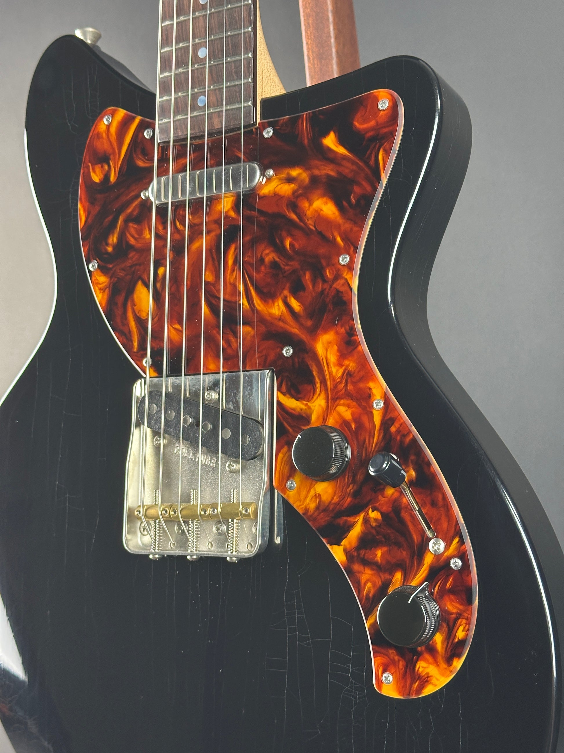 Close-up of a guitar with tortoiseshell pickguard and black body