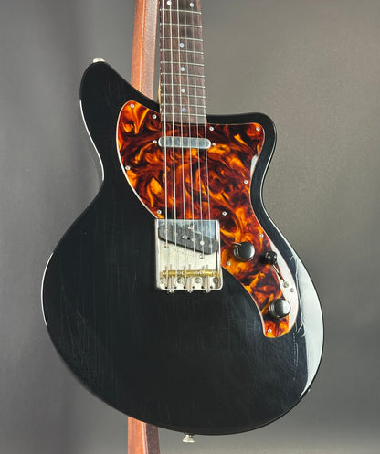 Black electric guitar with tortoiseshell pickguard on a gray background
