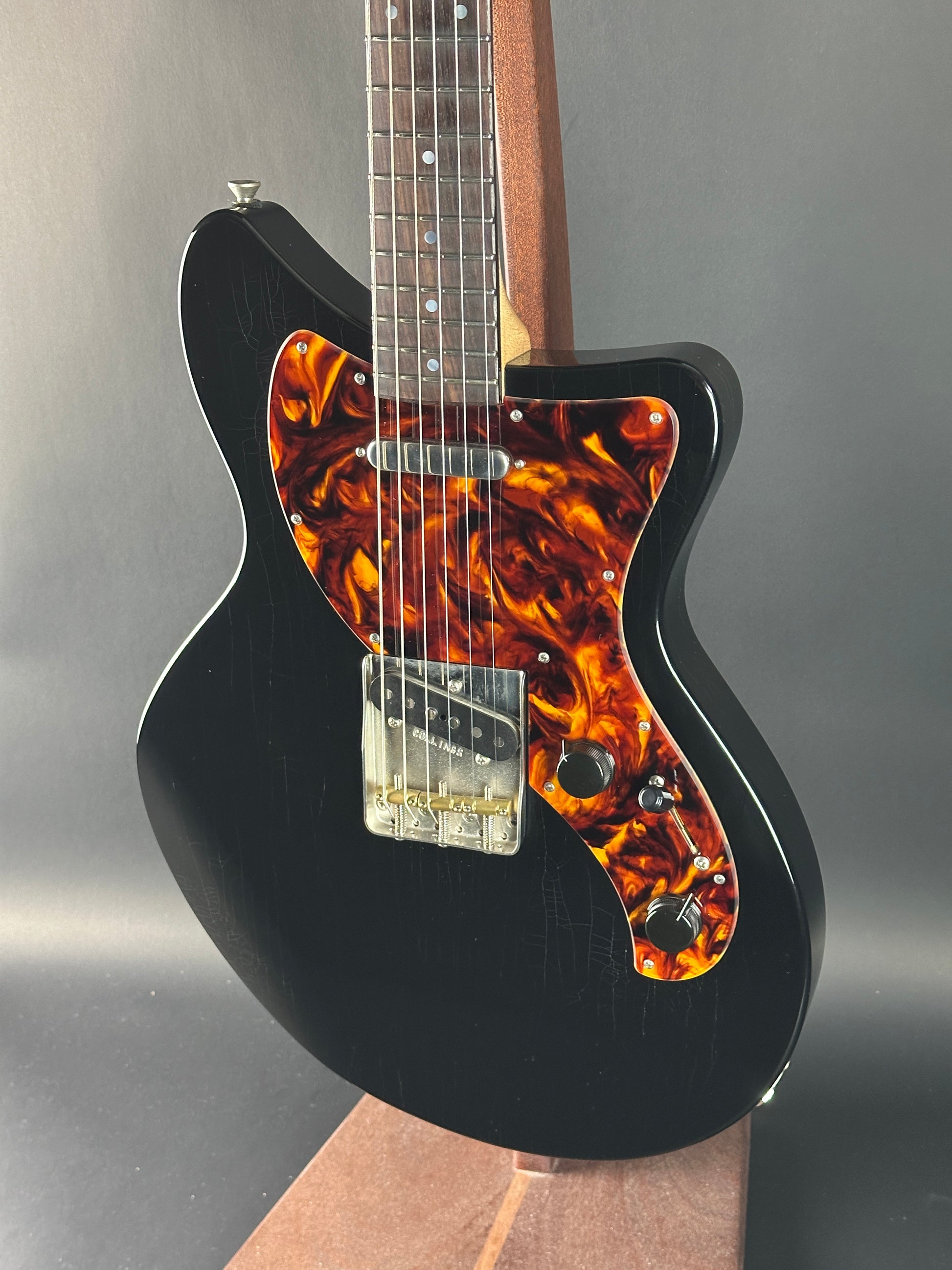 Black electric guitar with tortoiseshell pickguard on a gray background