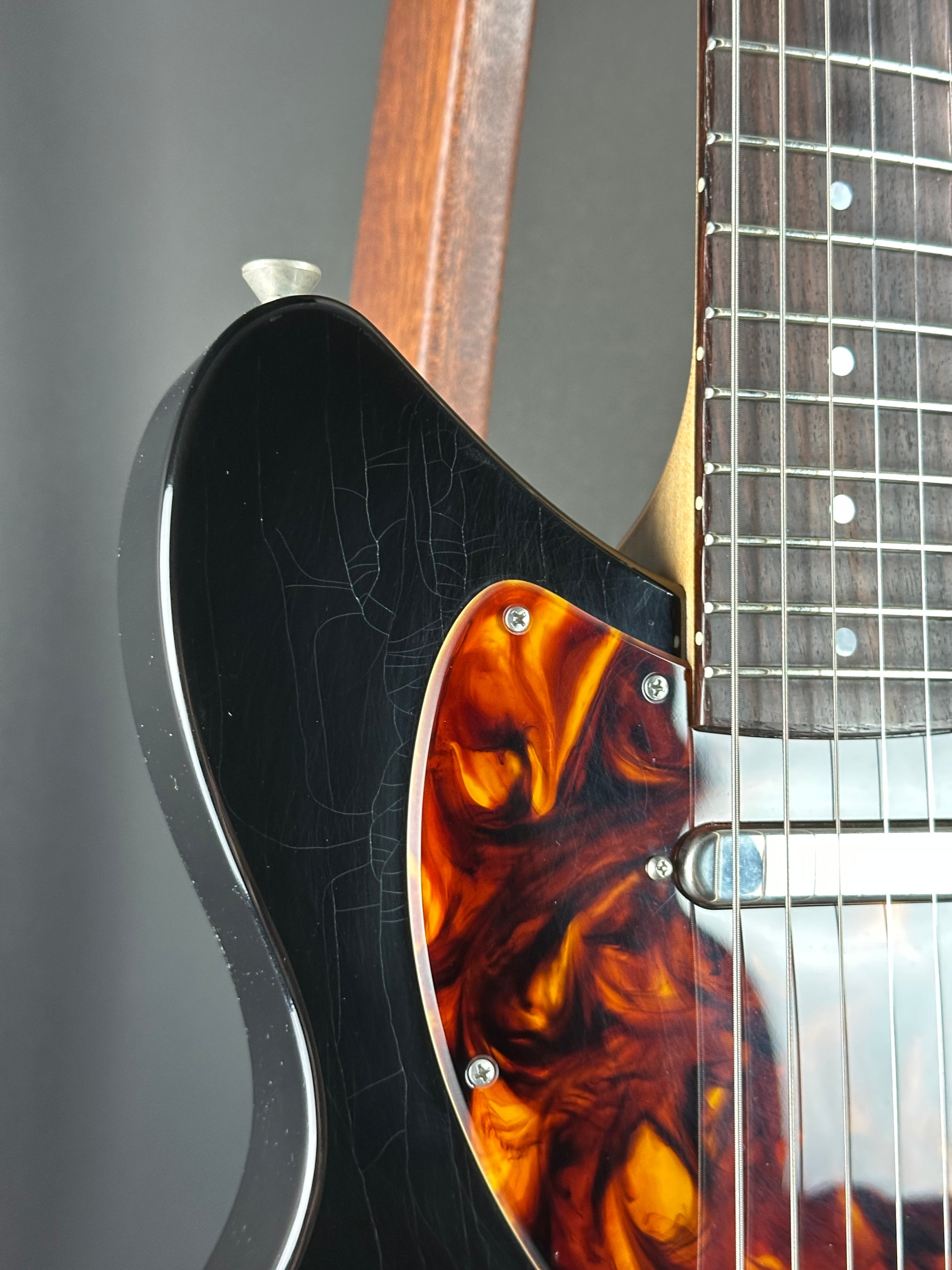 Close-up of a guitar's headstock with tortoiseshell design on a gray background