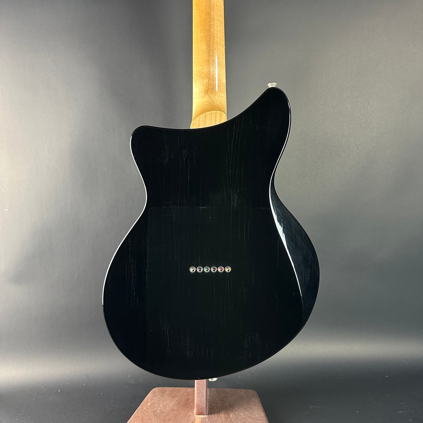 Black electric guitar on a stand against a gray background