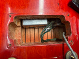 Close-up of a vintage red electric guitar's headstock interior, showing the silver metal logo plate, wooden slats, a dark green cord, and a silver cable.