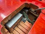 Close-up of a red electric guitar body showing the soundhole, a silver metal pickup, a green cable, and a wooden fingerboard.