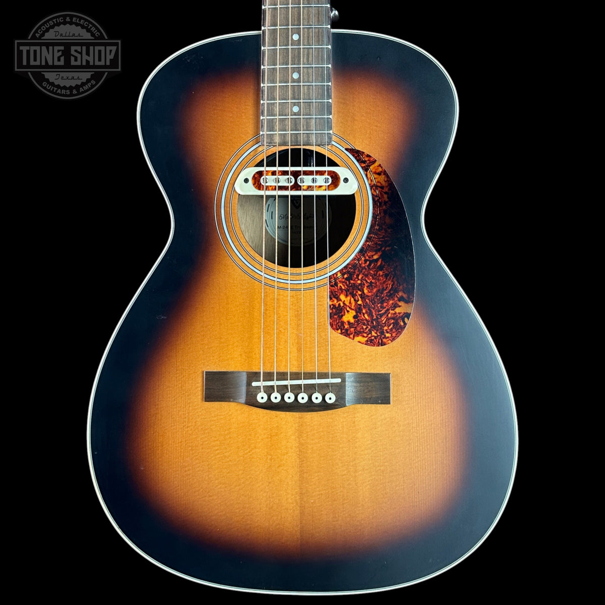 Acoustic guitar with a sunburst finish on a black background, featuring the Tone Shop logo.