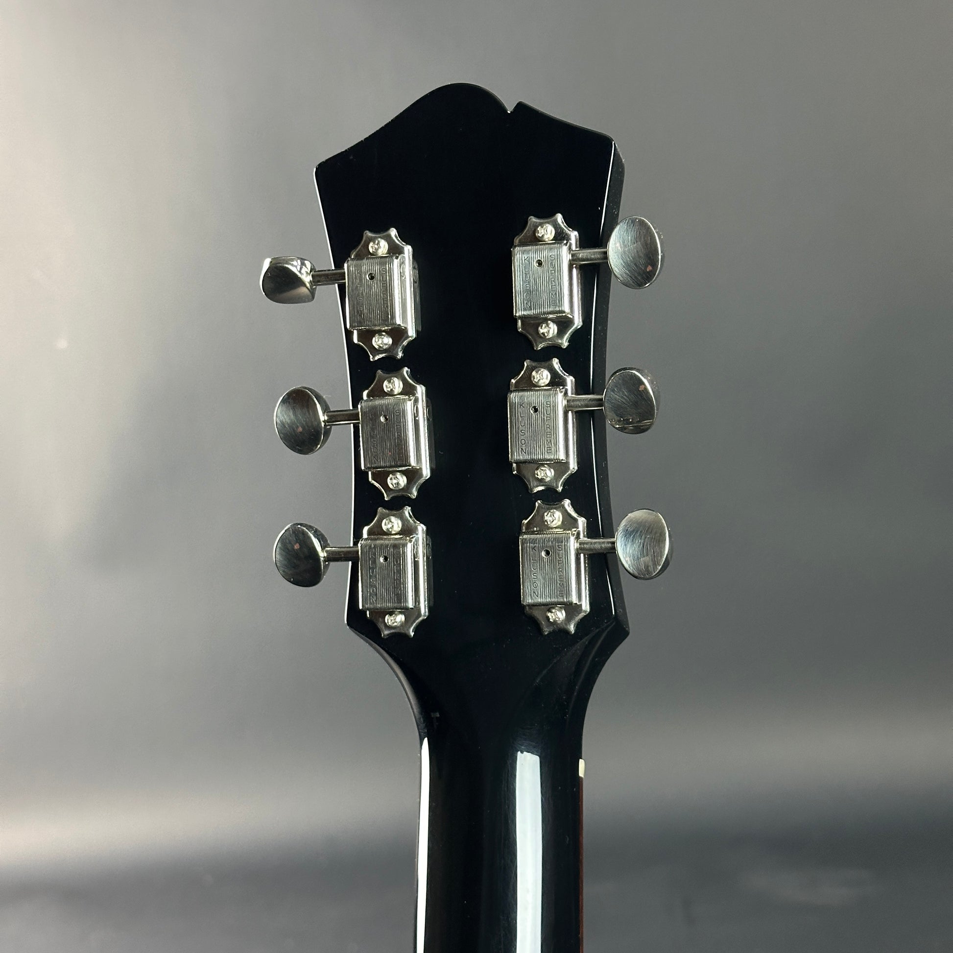 Close-up of a black guitar headstock with tuning pegs on a gray background