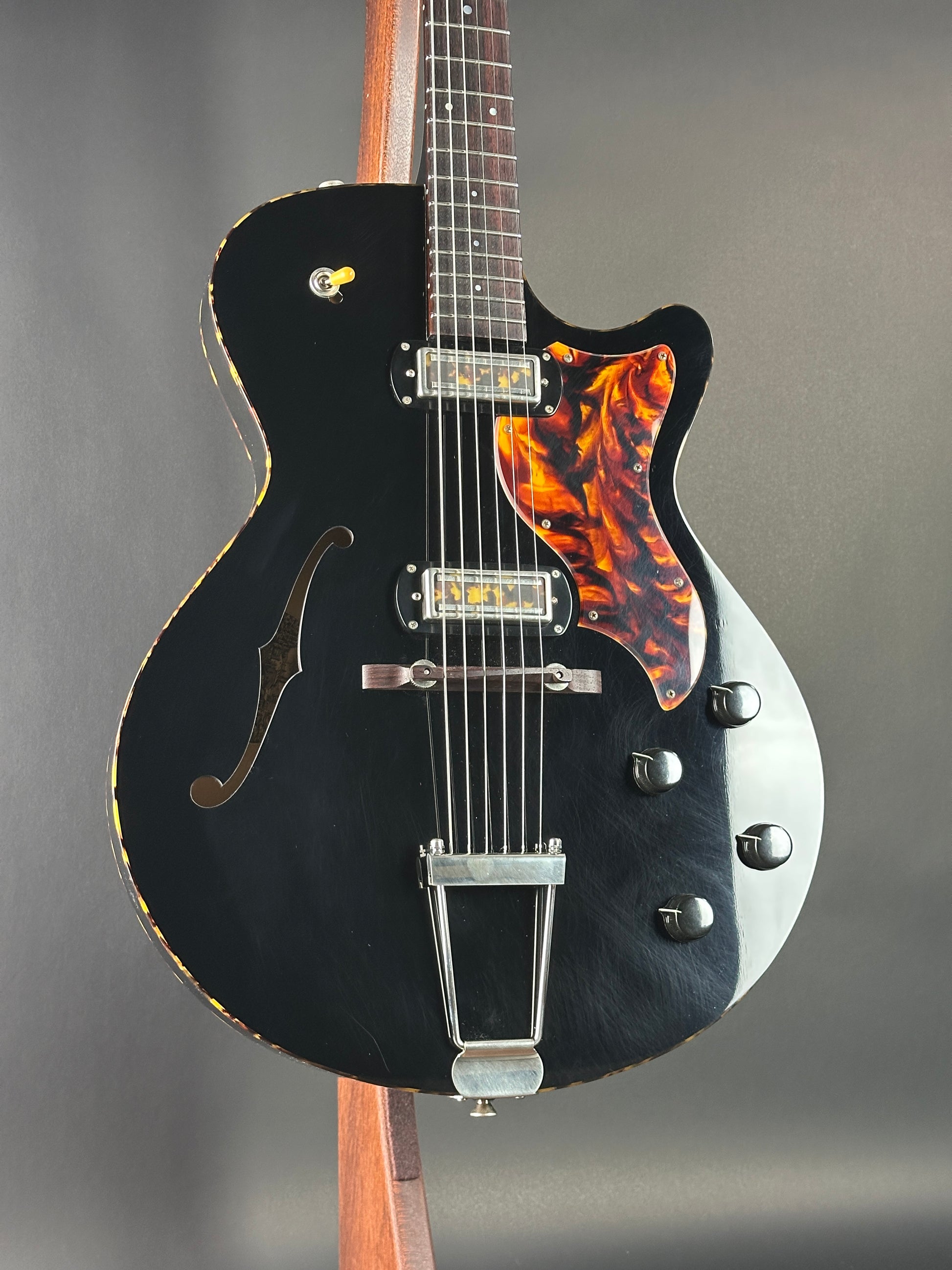 Black electric guitar with tortoiseshell pickguard on a gray background