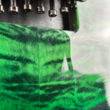 Close-up of a green and black tiger-stripe patterned vinyl wrap being applied to a guitar body by an embroidery machine.