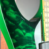 Close-up of a green electric guitar body showing a glossy flamed maple wood finish, part of the neck, and a pickup.