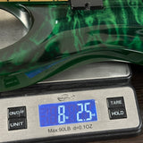 A close-up of a green marbled or woodgrain object resting on a digital scale, with the scale display reading 8.25 oz.