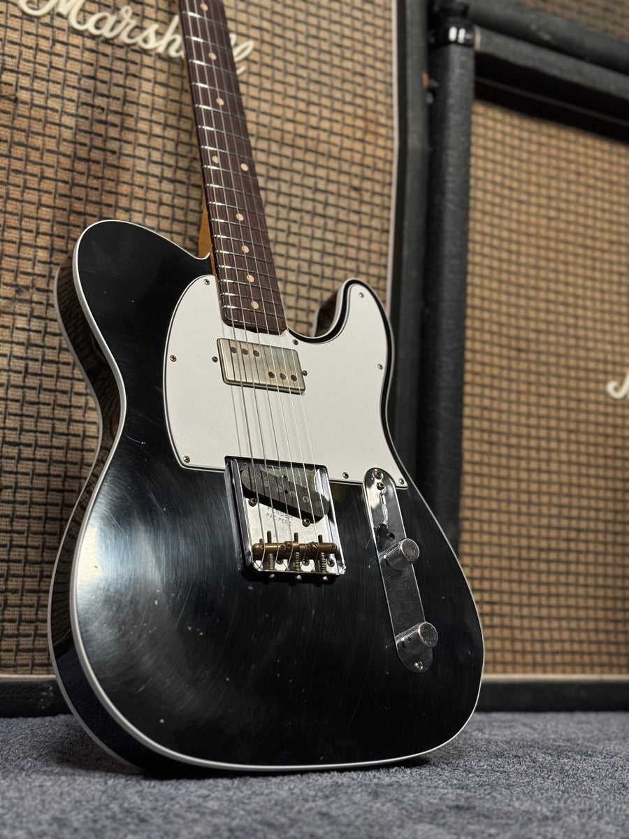 Black telecaster guitar leaning against a stack of marshall amplifiers with basketweave grills.