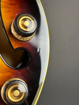 Close-up of a guitar body showing two gold-and-black volume/tone controls and part of a sunburst finish against a dark gray background.