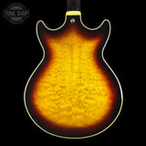 The back of an electric guitar with a classic sunburst finish, showing a vibrant flamed maple wood grain that transitions from bright yellow-orange in the center to a dark brown edge, set against a solid black background.