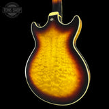 The back of an electric guitar with a classic sunburst finish, showing a vibrant yellow and orange flame pattern on the back, set against a solid black background.