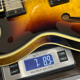 Close-up of a guitar body resting on a digital scale to measure weight, with the scale displaying 7.89 lbs.