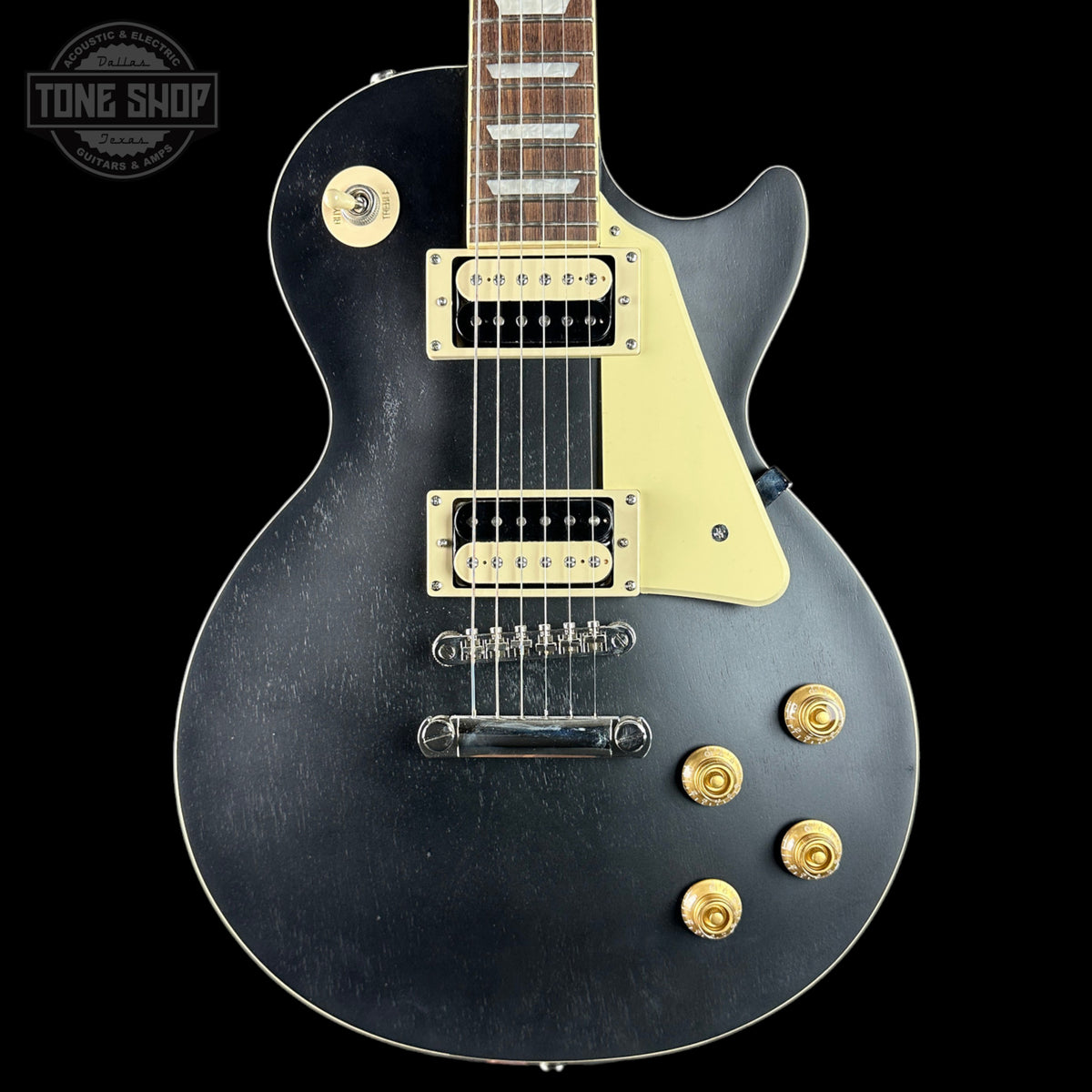 Black electric guitar with gold hardware on a black background, featuring 'Tone Shop' logo.