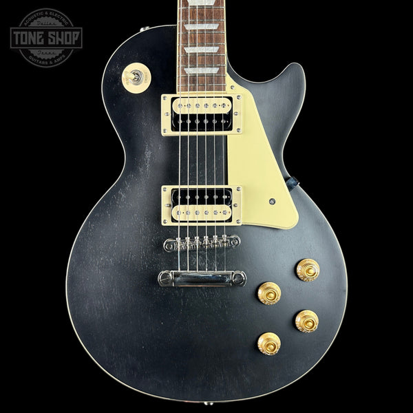 Black electric guitar with gold hardware on a black background, featuring 'Tone Shop' logo.