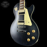 Black electric guitar with gold hardware on a black background, featuring 'Tone Shop' logo.